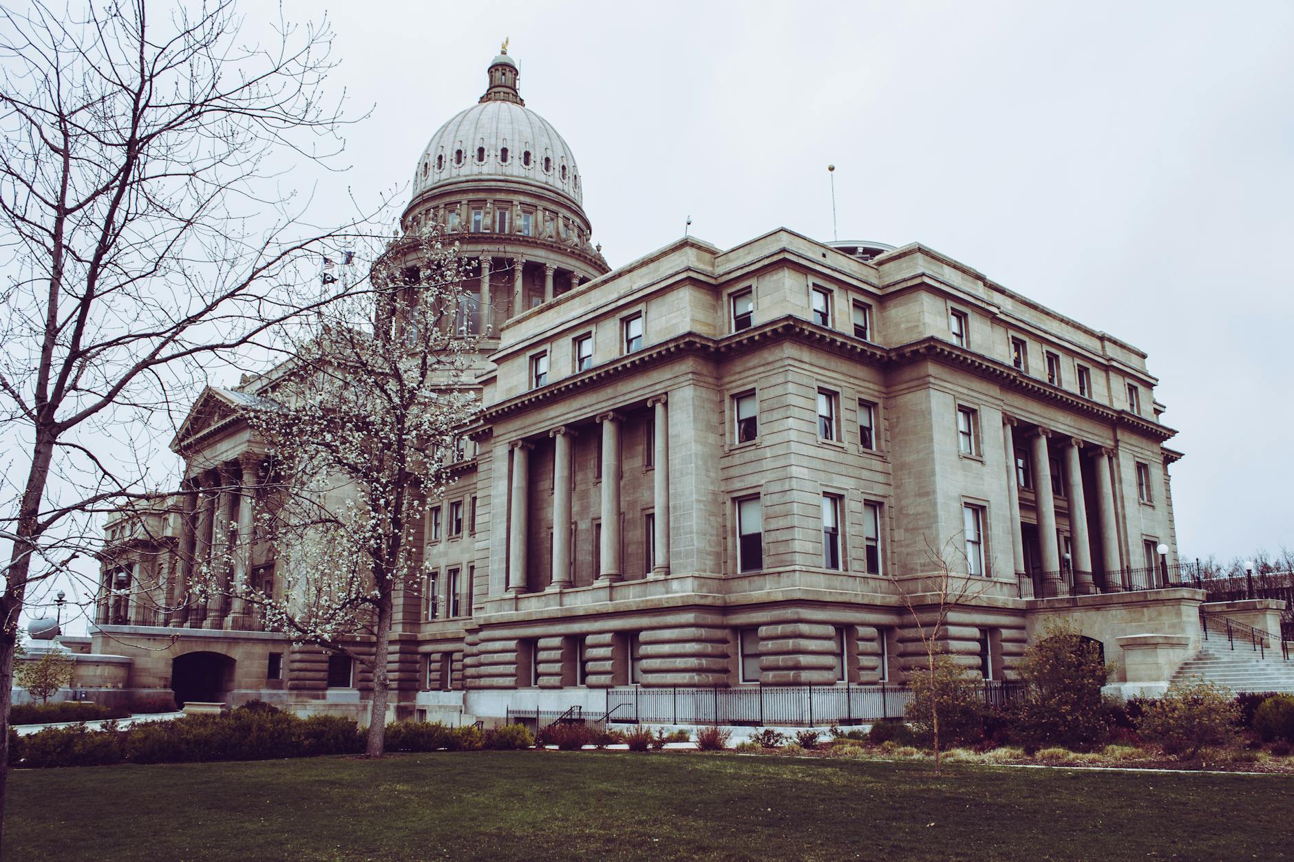A grand historic government building featuring a large dome and classical architectural elements, surrounded by greenery and bare trees.